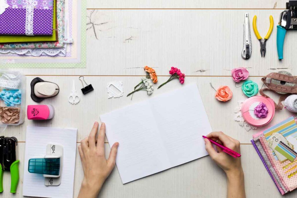 A person with a blank scrapbook sheet surrounded by flowers and other scrapbooking supplies