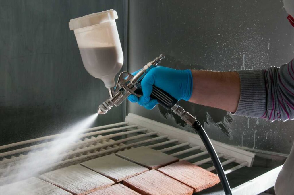 A person using a spray gun to spray glaze onto pottery tiles