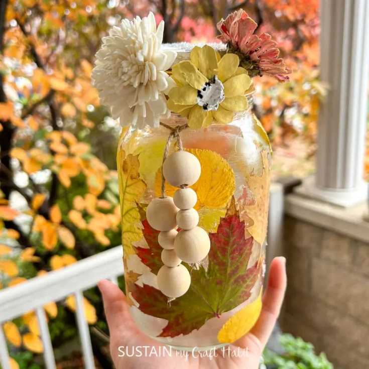 A fall luminary made out of glass jar, leaves, flowers, and beads