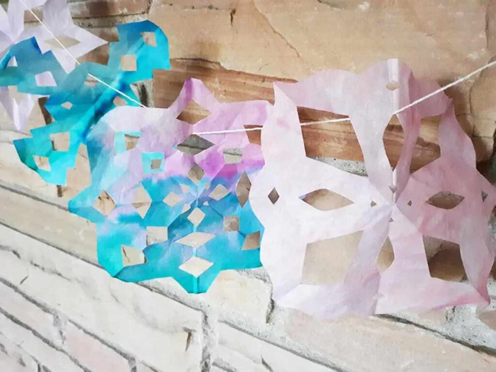 Snowflakes made out of coffee filters and hung on a fireplace mantle