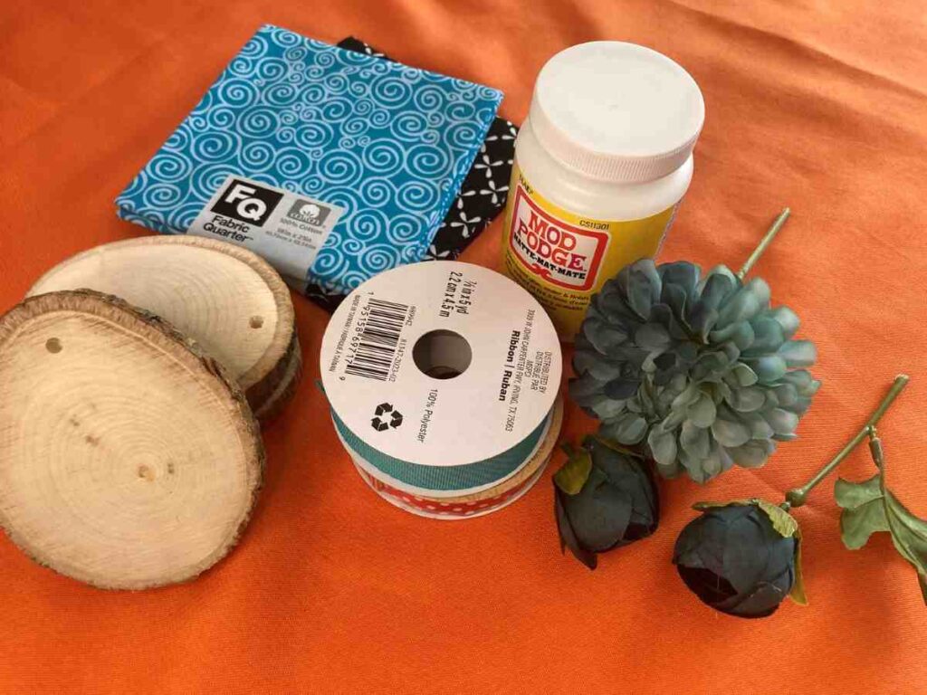 Supplies for wood slice ornament including fabric, ribbons, and mod podge