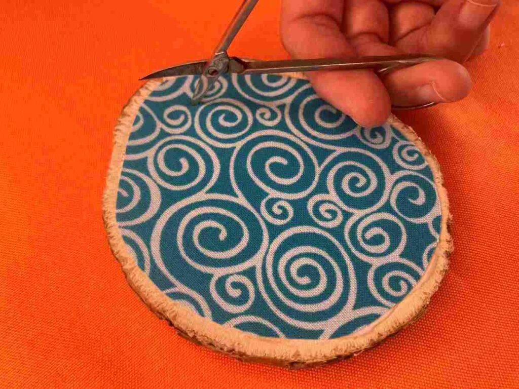 Using a small pair of scissors to cut a hole in fabric for a wood slice ornament