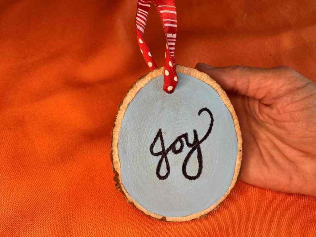 A wood slice ornament painted blue with the word JOY in black
