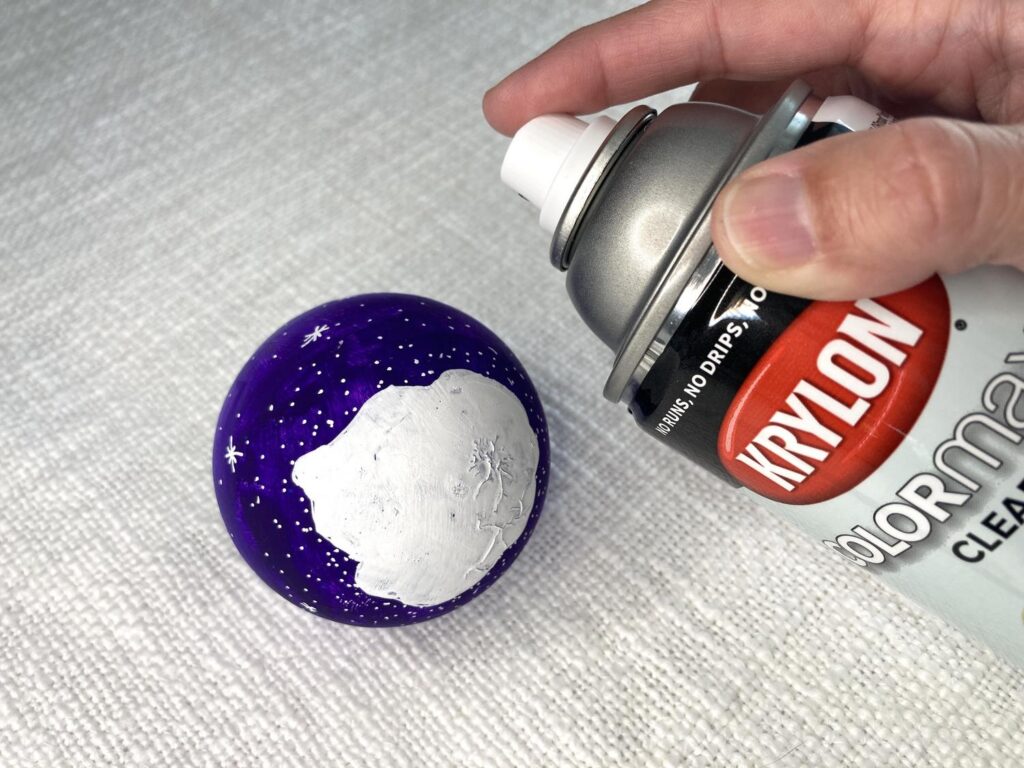 Spraying sealant on a hand painted ornament