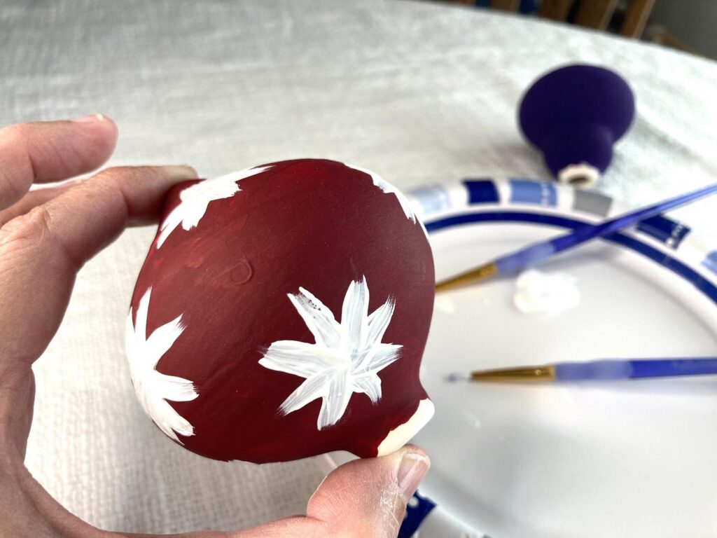 Painting white snowflakes on a red Christmas ornament
