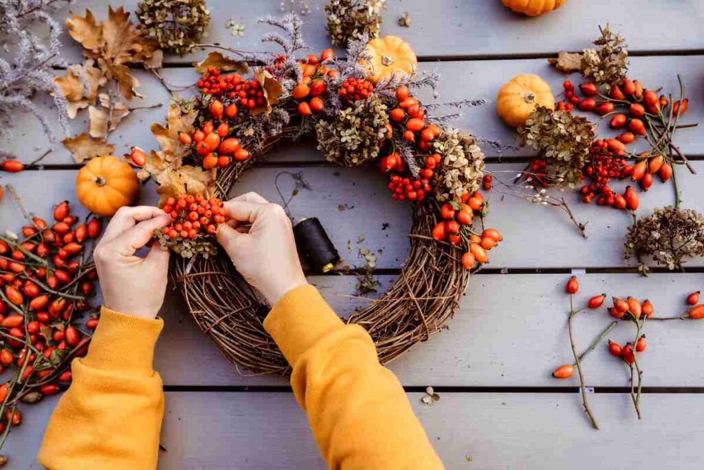 A person making a fall wreath with berries and pumpkins, fall craft ideas